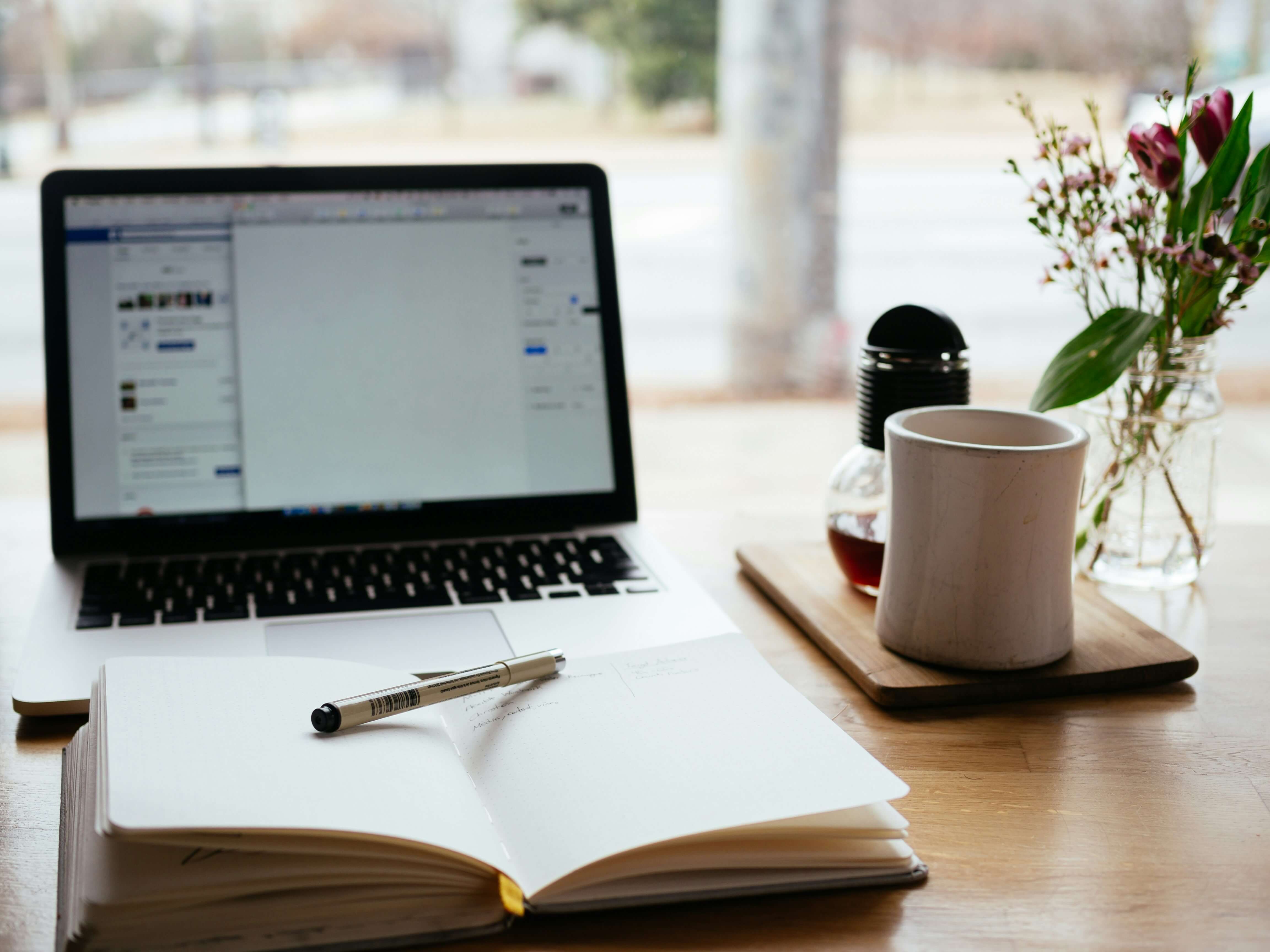 Notepad, pen and coffee cup in front of a laptop